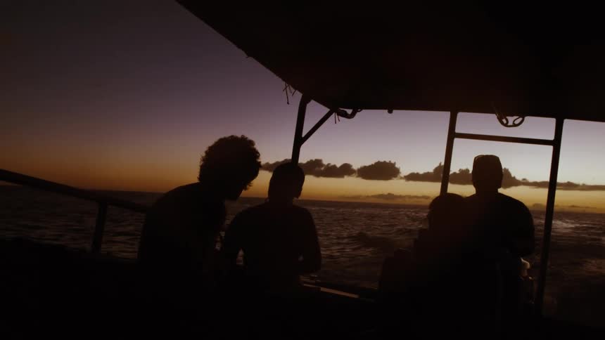 Silhouettes of people on a boat sailing across the ocean during a beautiful sunset