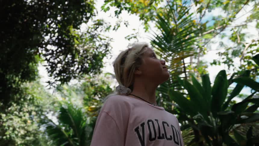 Slow motion, low angle shot of a young woman admiring the beauty of a lush tropical forest