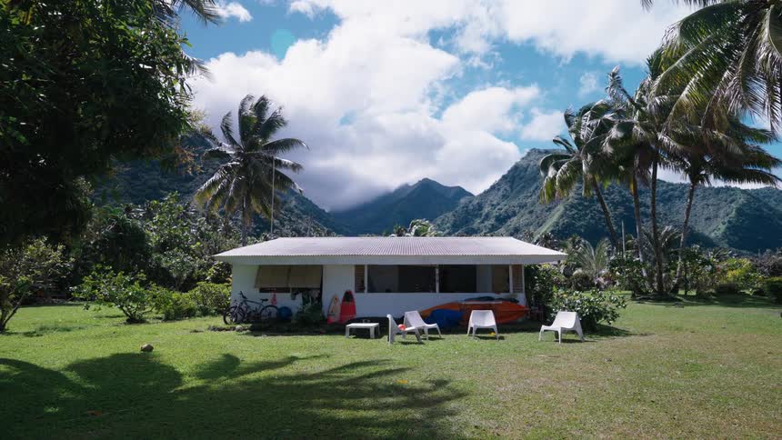 A peaceful vacation home sits in a tropical paradise surrounded by palm trees and lush green mountains