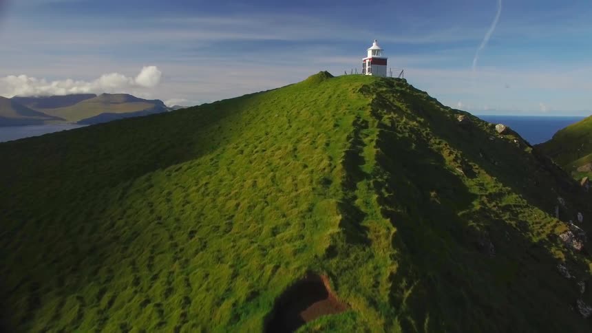 A man walks atop a hill towards a lighthouse