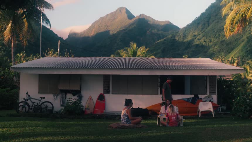 A group of friends relaxes outside their tropical bungalow at the base of a lush green mountain range