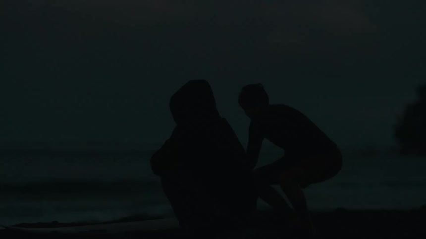 A moody silhouette shot of two surfers preparing their gear on the beach at dawn or dusk
