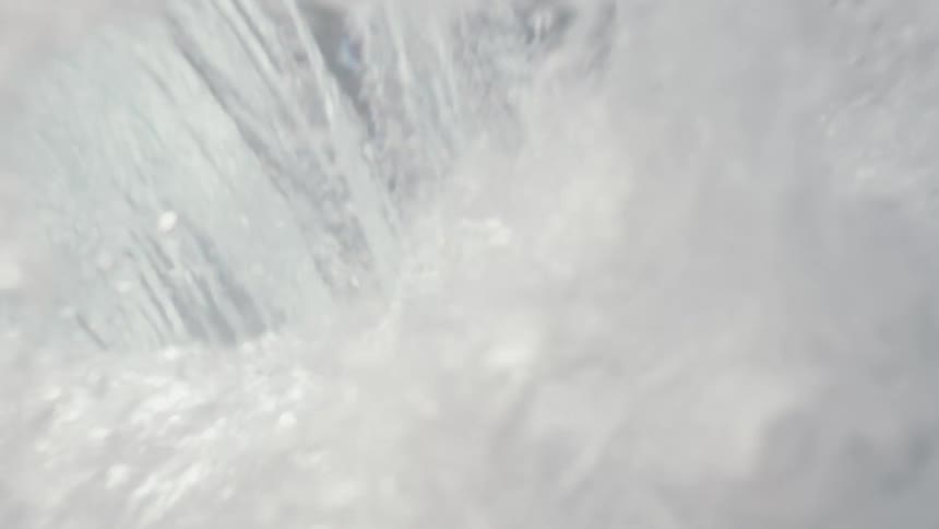 Slow motion, low-angle shot of a surfer riding a wave directly towards the camera before being engulfed by the crashing water