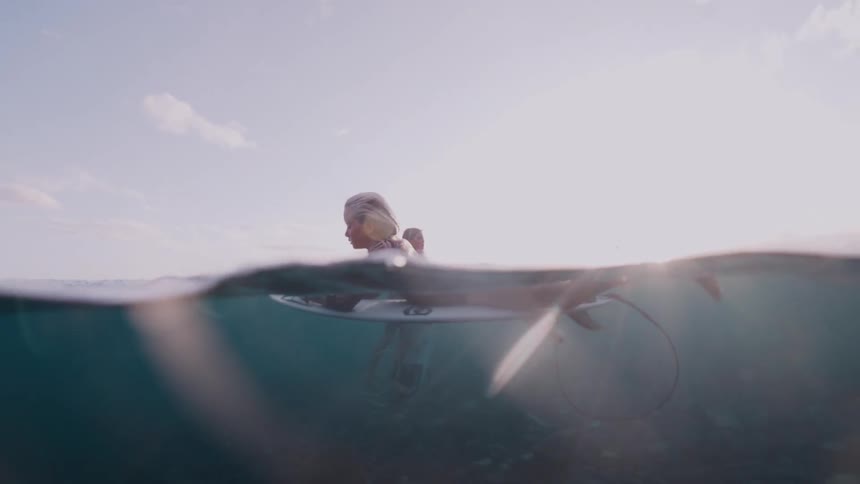 A serene split-level underwater and above water view of a female surfer waiting on her board in the ocean