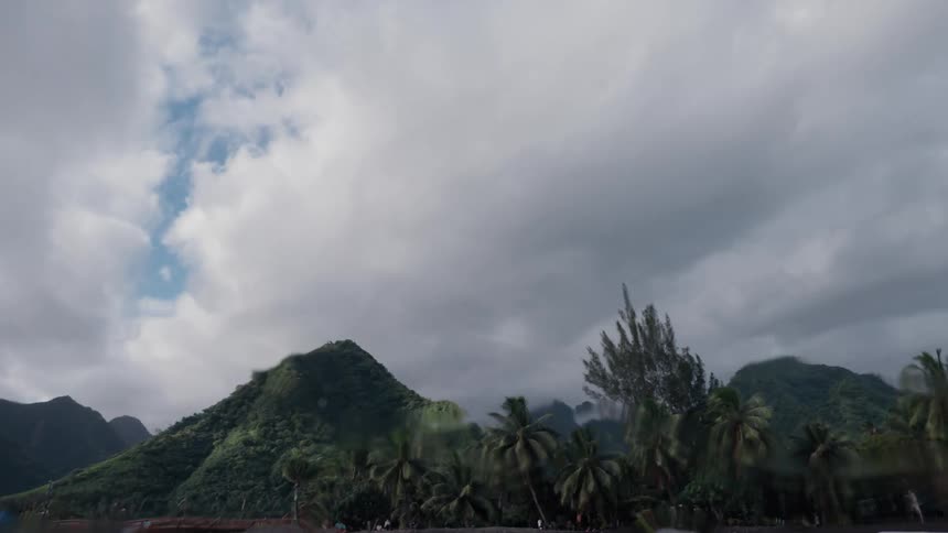 Slow motion shot emerges from the ocean to reveal a dramatic tropical island with lush green mountains and a black sand beach