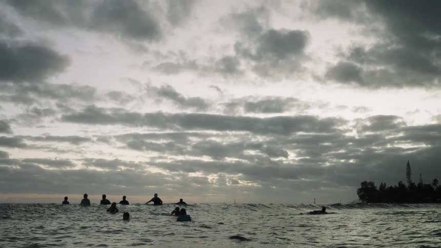 A group of surfers silhouetted against the morning sky wait patiently for waves in the ocean