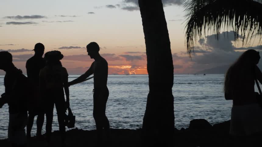 A group of friends enjoys a stunning tropical sunset over the ocean, silhouetted against the colorful sky