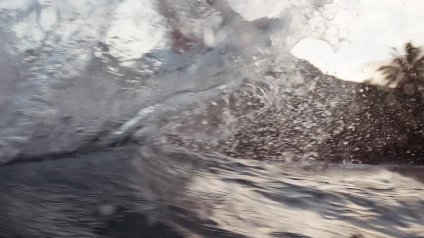 A determined female surfer carves a wave with intense focus in a dramatic, slow-motion close-up shot that ends with a powerful splash