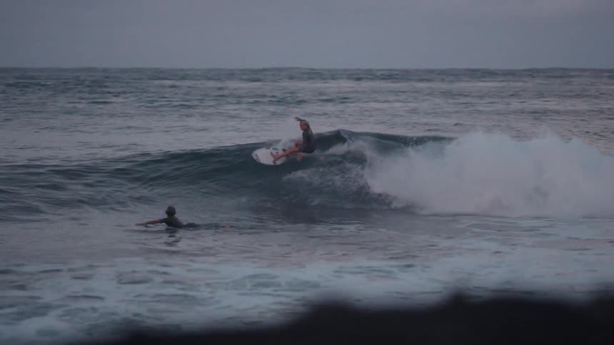 A skilled surfer in a wetsuit expertly rides along a breaking ocean wave in moody, overcast light