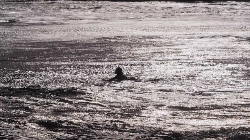 A lone person's silhouette is seen in the shimmering water as gentle waves pass by