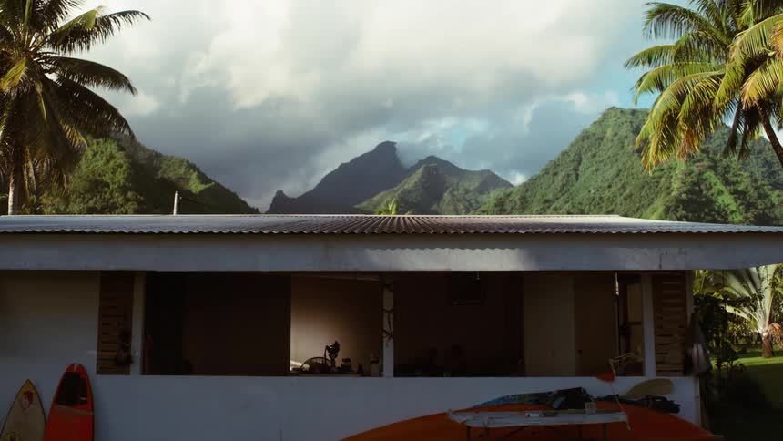 Serene view of a tropical island home nestled beneath dramatic green mountains and cloudy skies