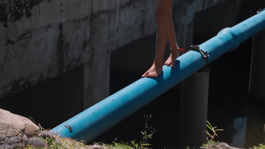 Close up of a young girl's bare feet as she carefully walks and balances across a large blue pipe