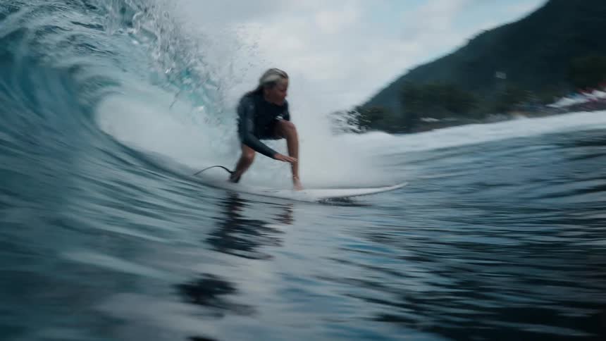 A skilled female surfer expertly rides inside the barrel of a powerful ocean wave in stunning slow motion