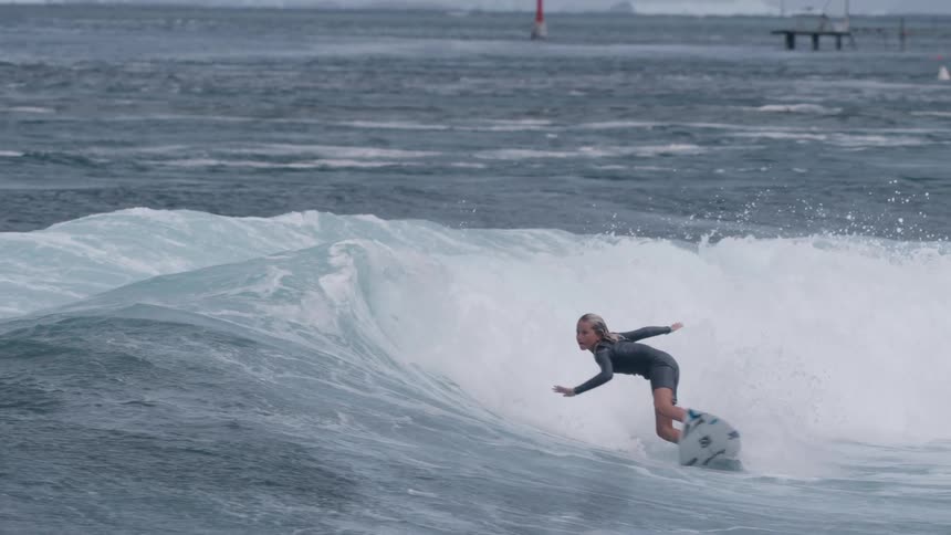 A skilled young female surfer gracefully carves a wave, creating a dramatic spray in super slow motion