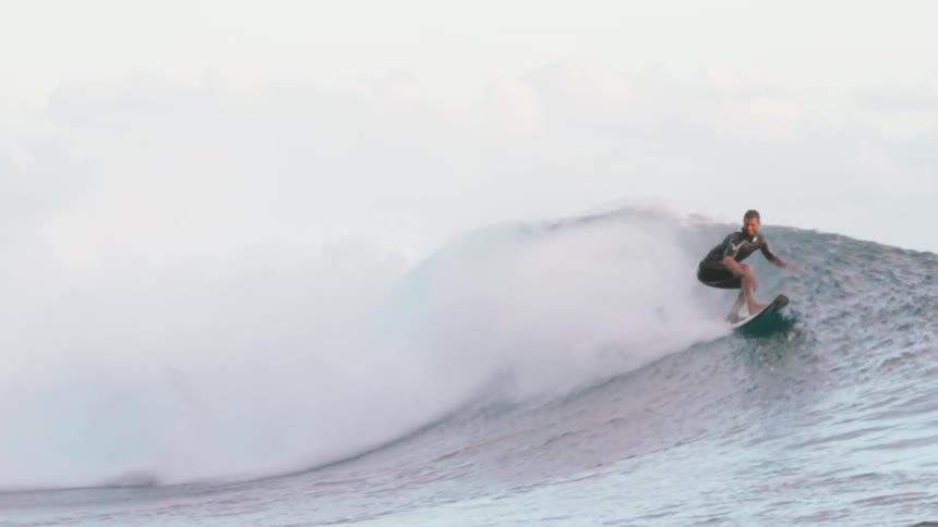 A professional surfer expertly rides a massive turquoise ocean wave in stunning slow motion