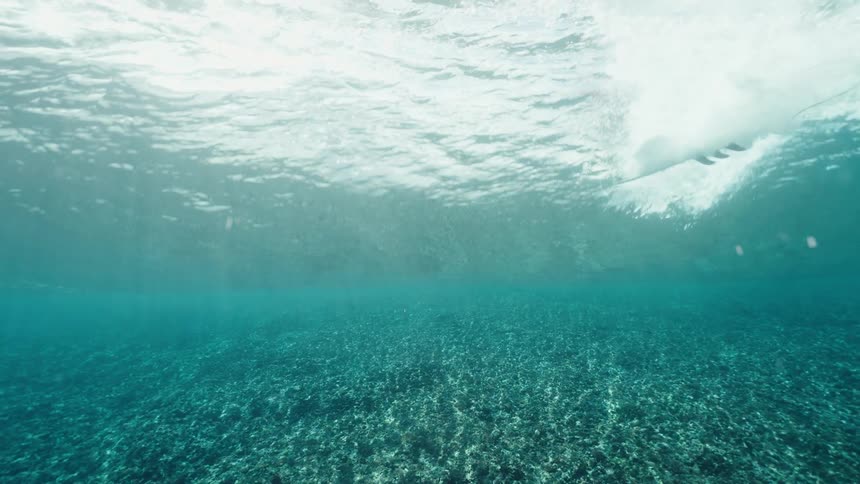Slow-motion underwater perspective of a surfer gliding on a crystal clear turquoise wave over a shallow reef