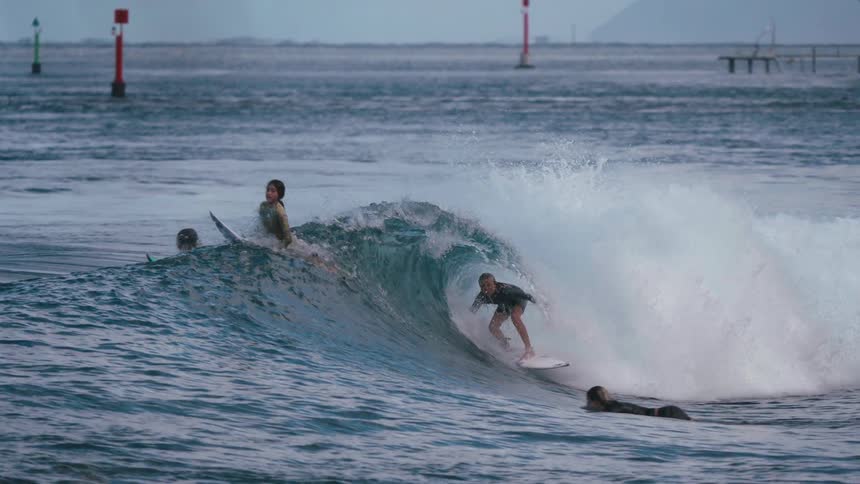 A surfer rides inside the barrel of a breaking wave in super slow motion as other people watch from the water