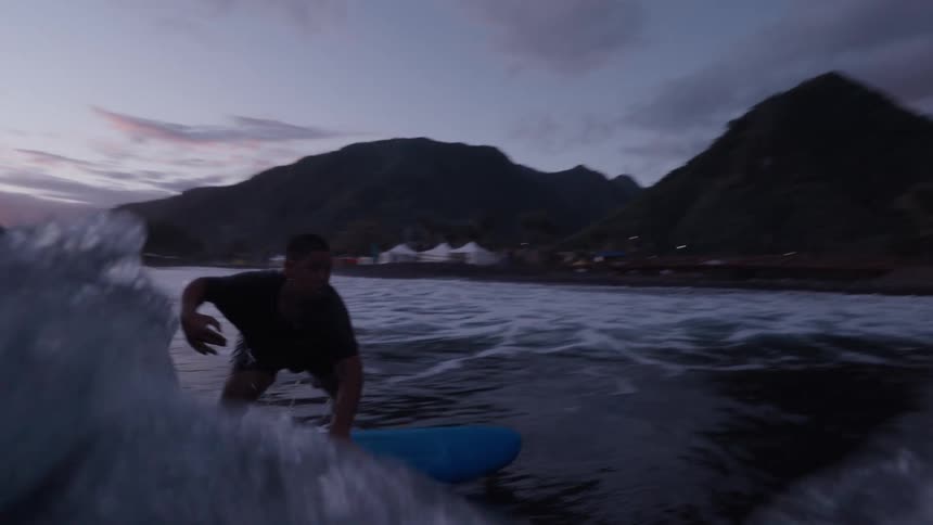 Dramatic slow-motion view of a surfer carving a wave at sunset, captured from an immersive perspective that goes underwater