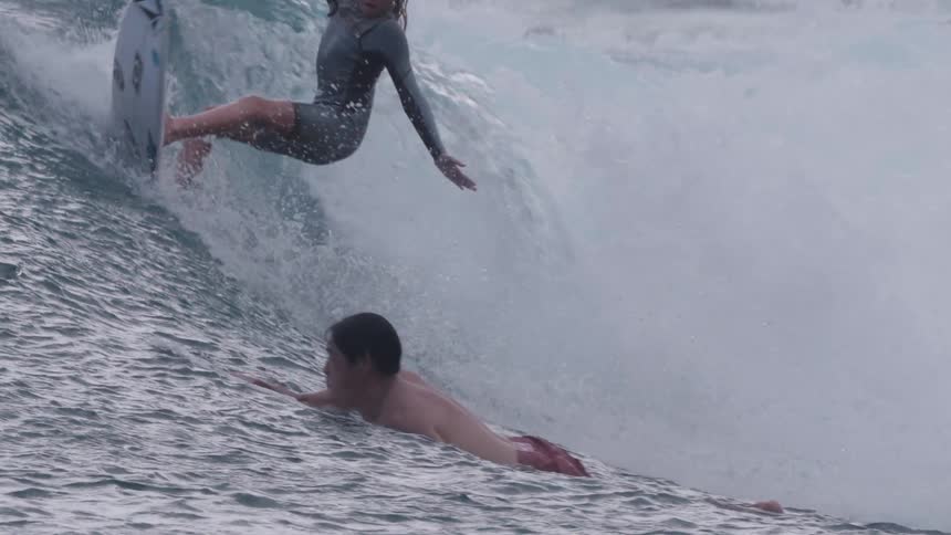 A skilled young female surfer expertly carves down the face of a rolling ocean wave in dramatic slow motion