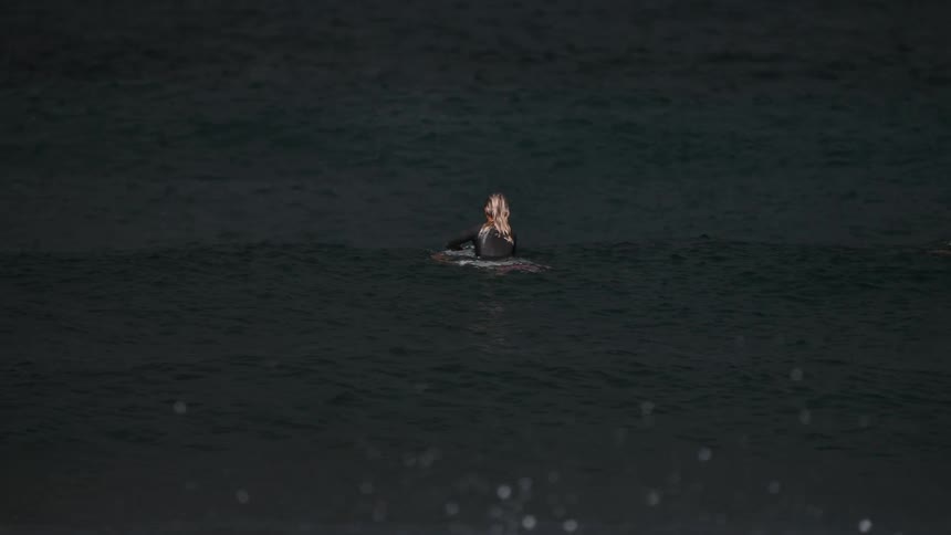 A blonde surfer patiently waits on her board in the dark ocean waters for the perfect nighttime wave