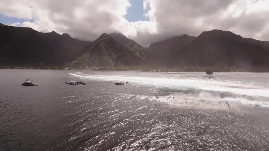 Slow motion aerial footage captures a perfect, powerful wave breaking in the ocean off a mountainous tropical island