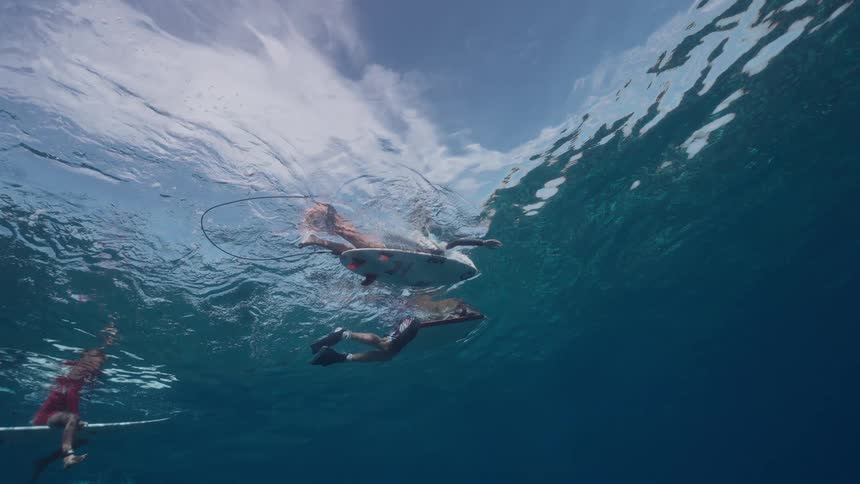 Unique underwater perspective shows surfers waiting patiently on their boards in tranquil blue water