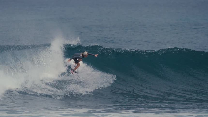 A surfer with long blonde hair gracefully rides a powerful ocean wave, carving a sharp turn in super slow motion