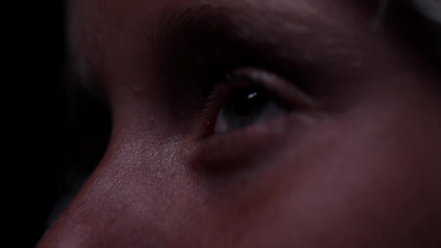 Extreme close-up on a person's eye as they blink slowly in a dark room