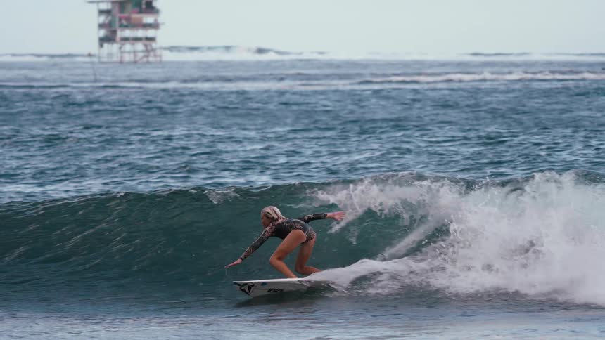 A young female surfer skillfully carves along a deep blue ocean wave in stunning slow motion, showcasing her balance and control before wiping out