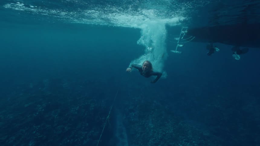 A woman in a wetsuit gracefully dives into the deep blue ocean from a boat in a slow motion underwater shot