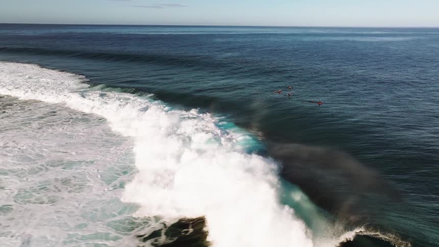 A stunning slow-motion aerial view captures a surfer riding a massive wave as its spray creates a beautiful rainbow in the deep blue ocean