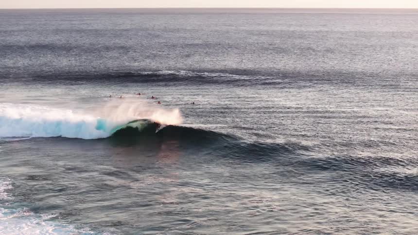 Slow motion wide shot of a surfer skillfully riding inside the barrel of a massive, peeling ocean wave during a serene sunset