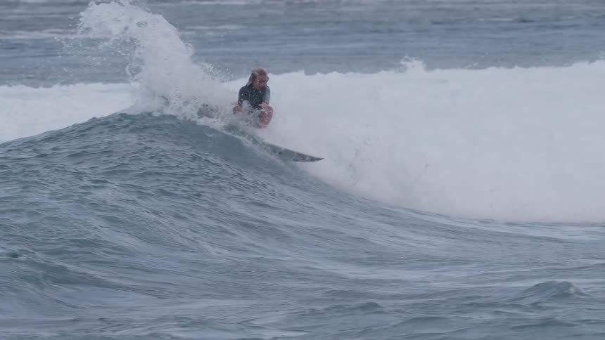 A skilled surfer expertly carves along a powerful ocean wave in super slow motion before being consumed by the whitewash
