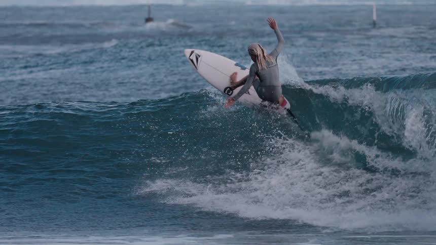 A young female surfer in a wetsuit skillfully catches a wave and executes a powerful turn on the water in dramatic slow motion