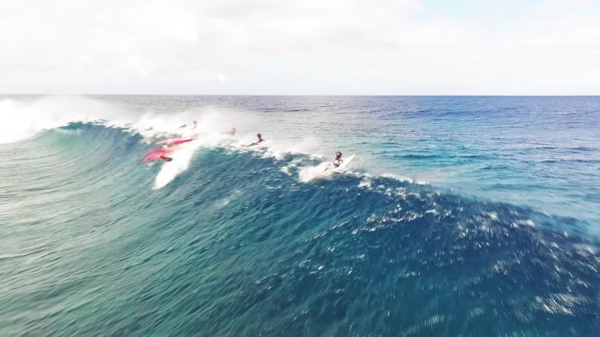 Stunning aerial footage follows a group of surfers as they all catch and ride a large, beautiful turquoise ocean wave