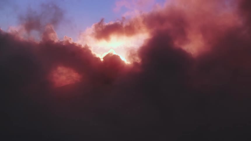 A beautiful but ominous sky shows the sun peaking through dark, reddish-purple clouds at sunset