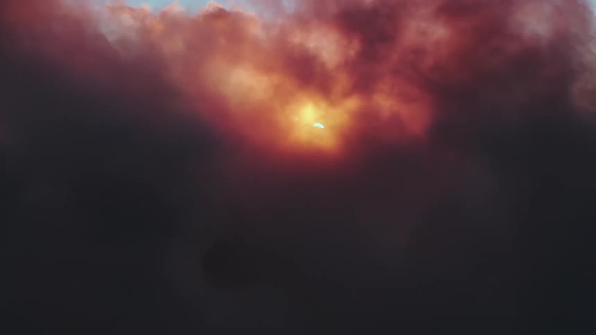 A dramatic time-lapse captures a solar eclipse as the sun slowly disappears behind thick, dark, reddish clouds