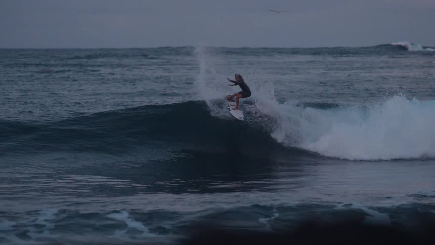 A surfer gracefully rides a dark ocean wave in stunning slow motion during a moody, overcast evening
