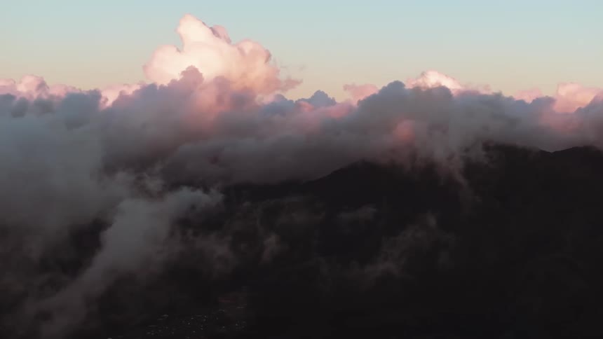 A static wide shot shows dramatic pink clouds floating over a silhouetted mountain range at dusk