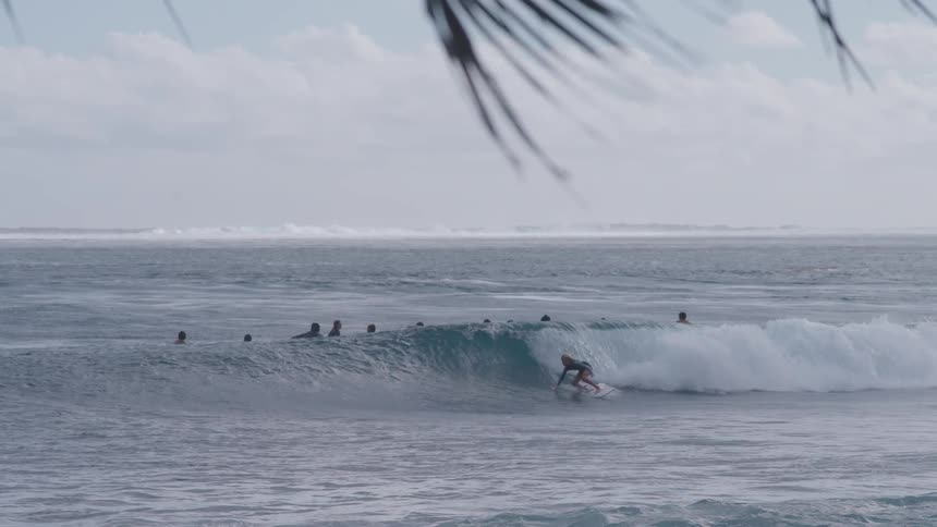 A group of surfers ride a long, rolling ocean wave one after another in beautiful slow motion