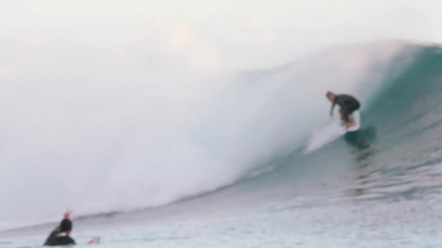 A skilled surfer expertly rides a massive turquoise barrel wave in slow motion as people watch from a boat