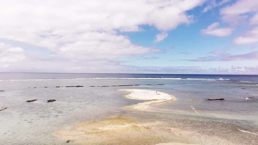 Aerial footage slowly flies over a tropical paradise with palm trees, a white sand beach, and a turquoise lagoon