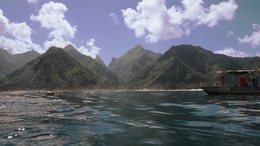 A tranquil water-level view of a tropical bay surrounded by lush green mountains with boats floating nearby