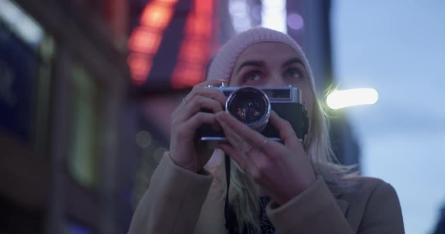 A woman takes a photograph on a city street at dusk