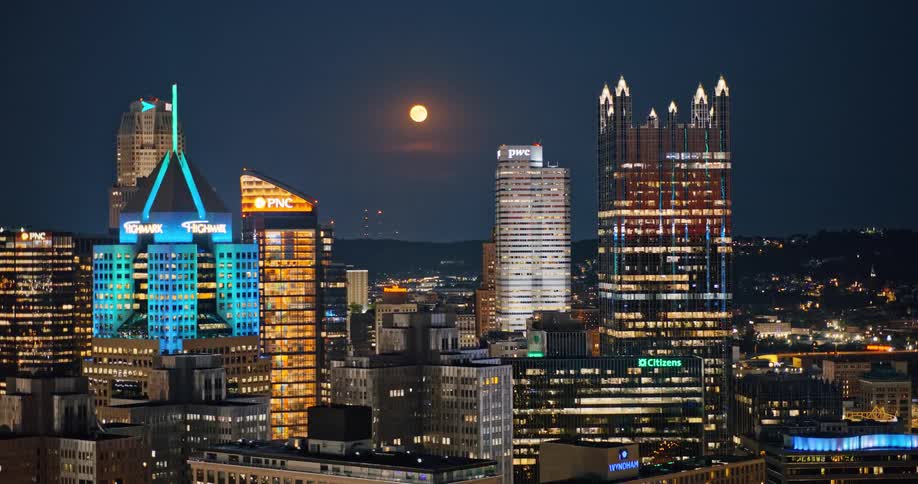 A beautiful static shot of the Pittsburgh, Pennsylvania skyline illuminated at night under a bright full moon