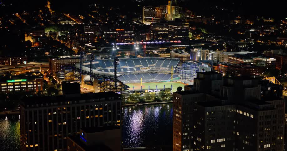 A slow aerial zoom out reveals the illuminated PNC Park baseball stadium and the Pittsburgh city skyline at night