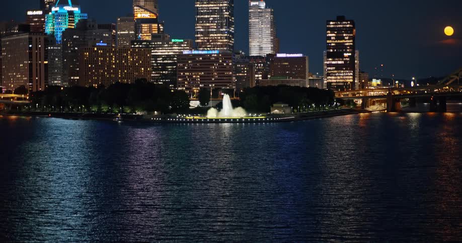 A slow tilt-up reveals the iconic Point State Park fountain and the Pittsburgh city skyline illuminated at night across the river