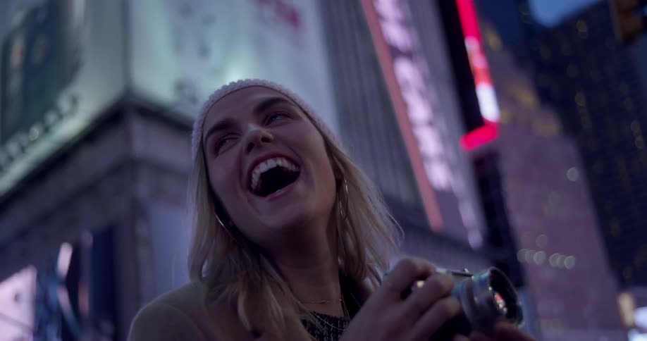 Woman smiling and taking pictures in a large city at night