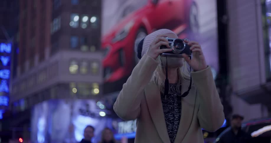 A woman takes a photograph in times square at night