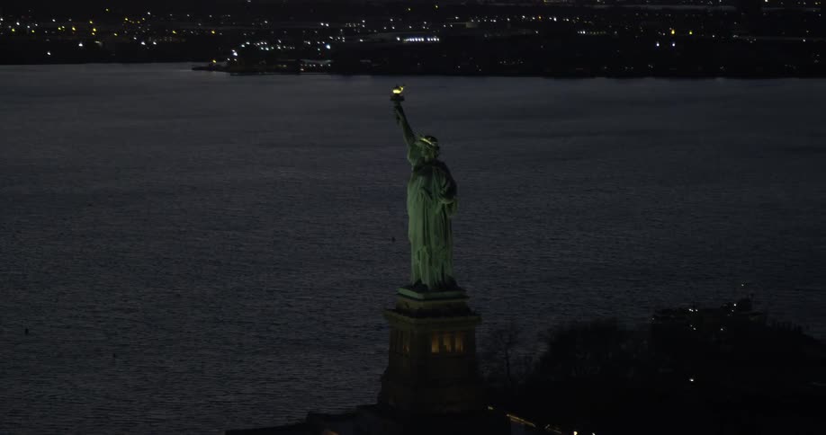 The statue of liberty stands lit up at night in new york harbor